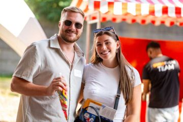 Julia Kötting with her husband. He is holding a bag of colourful lollipops; she is carrying a shoulder bag and holding some documents