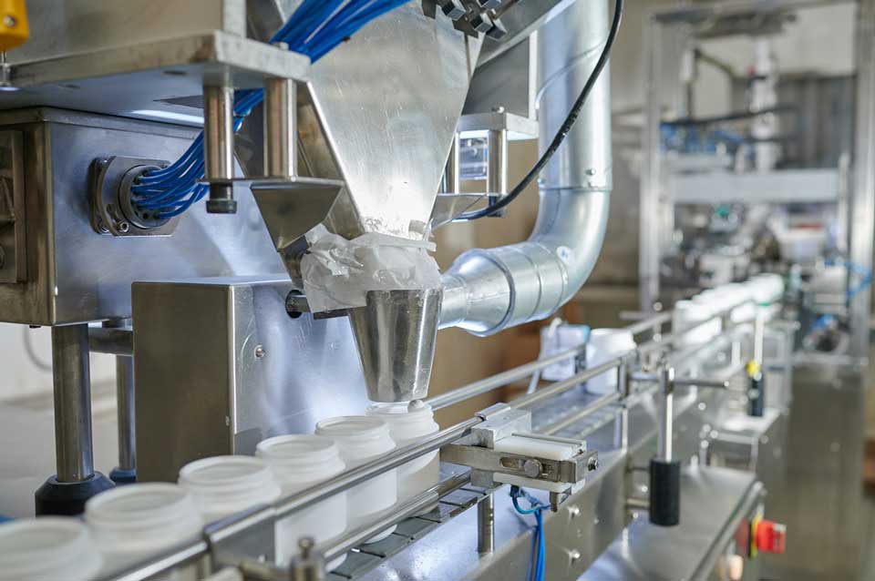 Maschine, die fertige Reinigungstabletten automatisiert in runde weiße Kunststoffdosen abfüllt