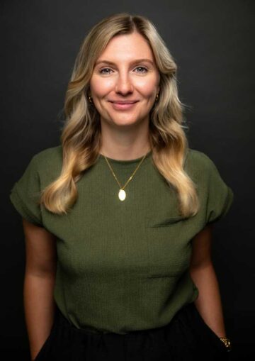 Portraitbild Maxi Hof. Sie hat lange blonde Haare und trägt ein grünes Oberteil. Sie lächelt sympathisch in die Kamera