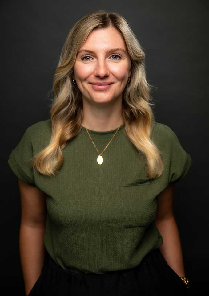 Portraitbild Maxi Hof. Sie hat lange blonde Haare und trägt ein grünes Oberteil. Sie lächelt sympathisch in die Kamera