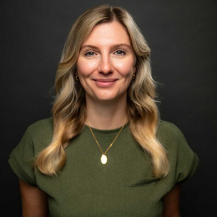 Portrait of Maxi Hof. She has long blonde hair and is wearing a green top. She is smiling warmly at the camera.